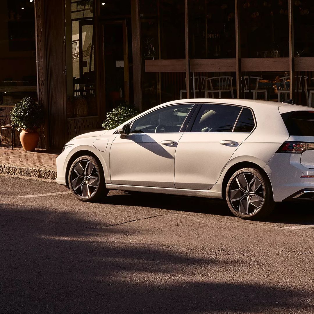 VW Golf Weißer Golf R-Line parkt seitlich vor einem Restaurant.