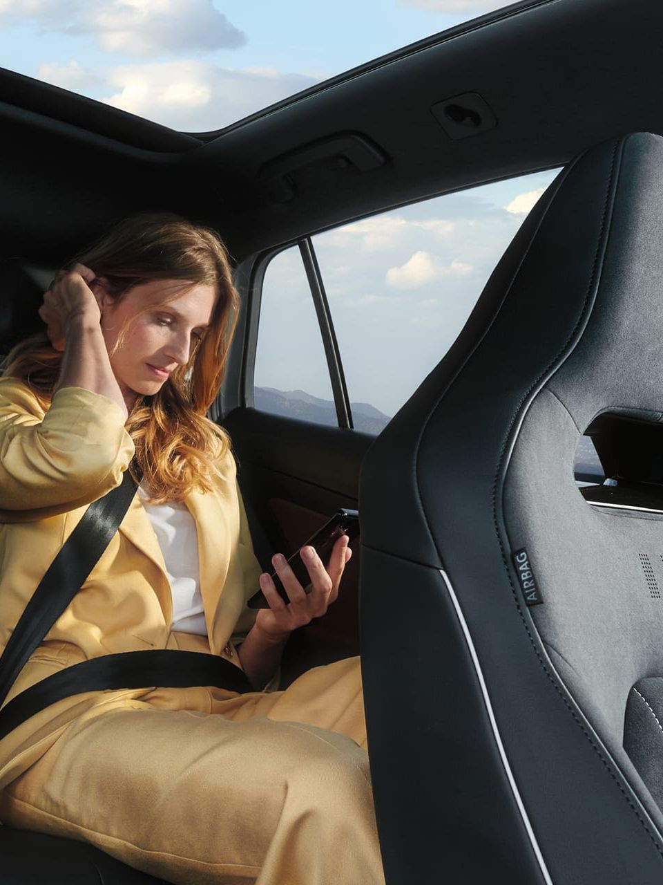 VW ID.5 Interieur, Blick auf die Rücksitzbank, Frau sitzt im Auto und schaut auf ihr Handy.