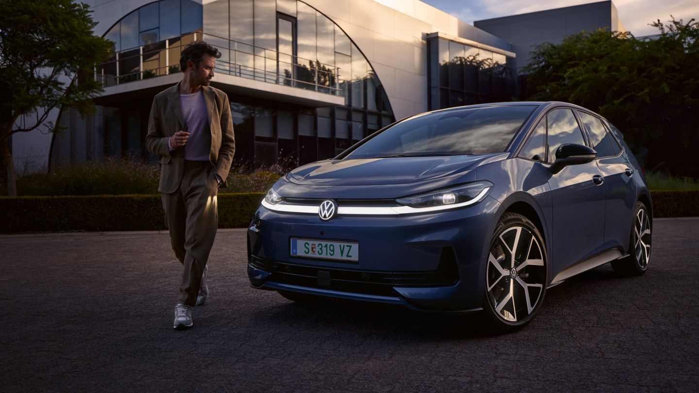 Ein Mann geht um die Front eines blauen VW ID.3 Neo und betrachtet das Lichtdesign