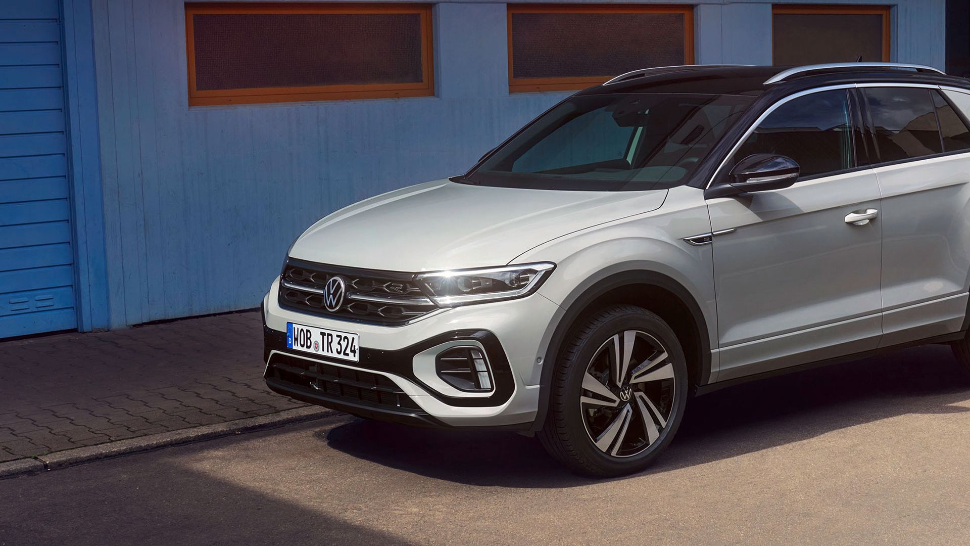 VW T-Roc R-Line in weiß vor einem Gebäude, Seite sichtbar, Mann fährt auf Skateboard vorbei