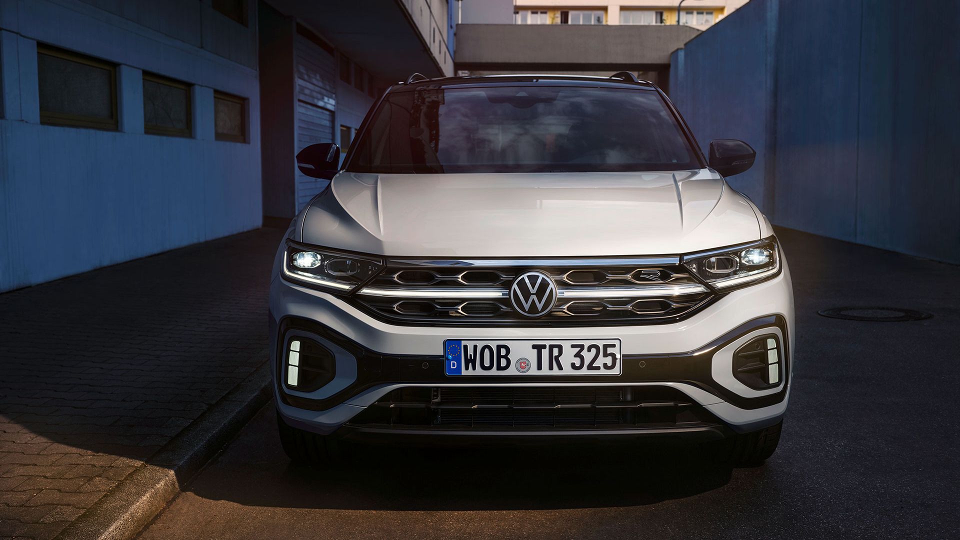 VW T-Roc R-Line Front in Weiß, LED-Tageslichtscheinwerfer und das optionale, illuminierte Kühlerschutzgitter leuchten