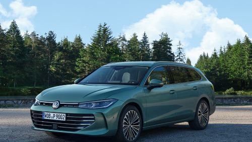 VW Passat in blaugrün steht auf einer Kiesfläche, das Gelände grenzt an einen Tannenwald.
