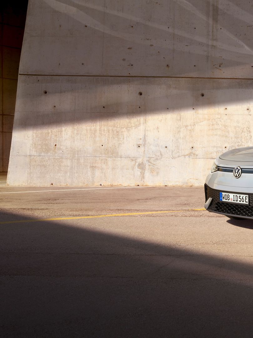 Grauer VW ID.5 parkt vor heller Hauswand, Ansicht schräg rechts von vorn, Mann geht zügig auf das E-Auto zu.