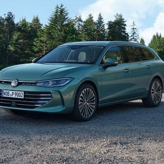 VW Passat in blaugrün steht auf einer Kiesfläche, das Gelände grenzt an einen Tannenwald.