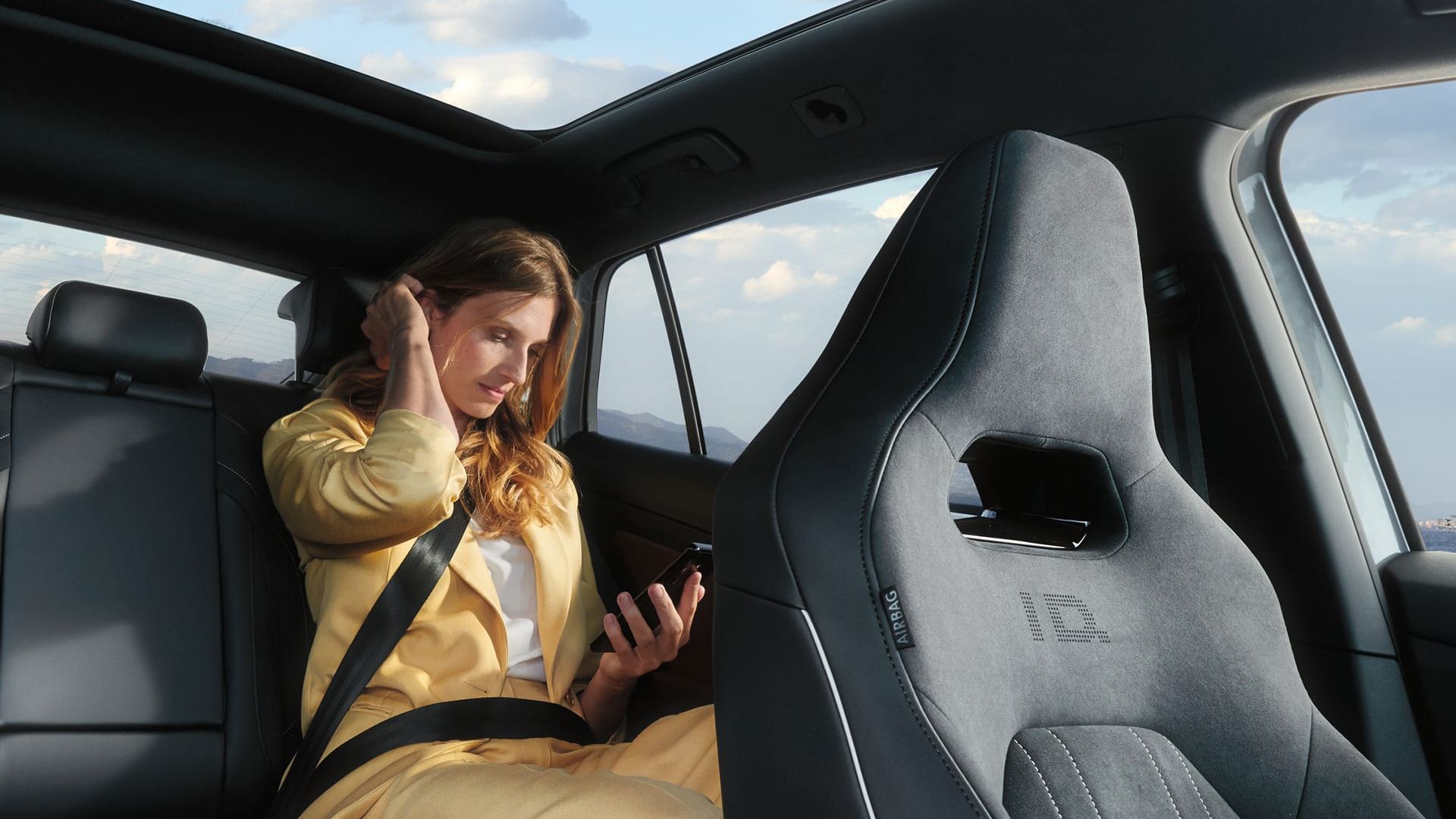 VW ID.5 Interieur, Blick auf die Rücksitzbank, Frau sitzt im Auto und schaut auf ihr Handy.