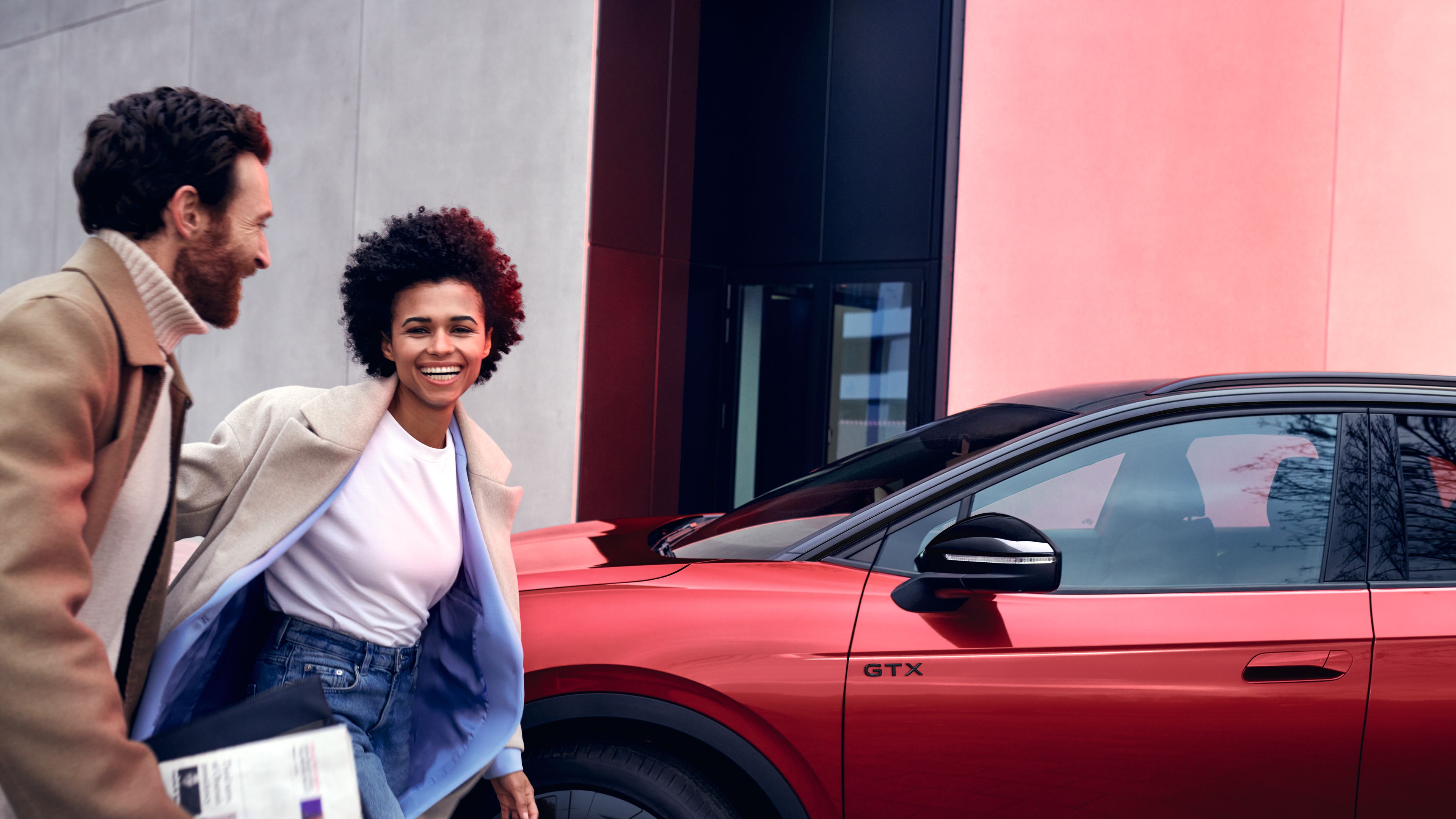 VW ID.5 GTX in Rot steht am Straßenrand, Seite der Front sichtbar, Frau und Mann gehen im Vordergrund vorbei